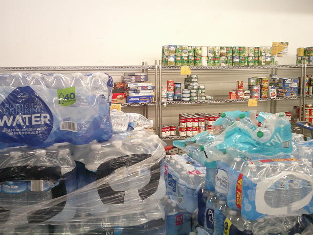 Pallets of water with shelves of canned goods behind them.